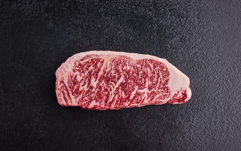 A wagyu beef steak, showing the marbling, on a dark background.